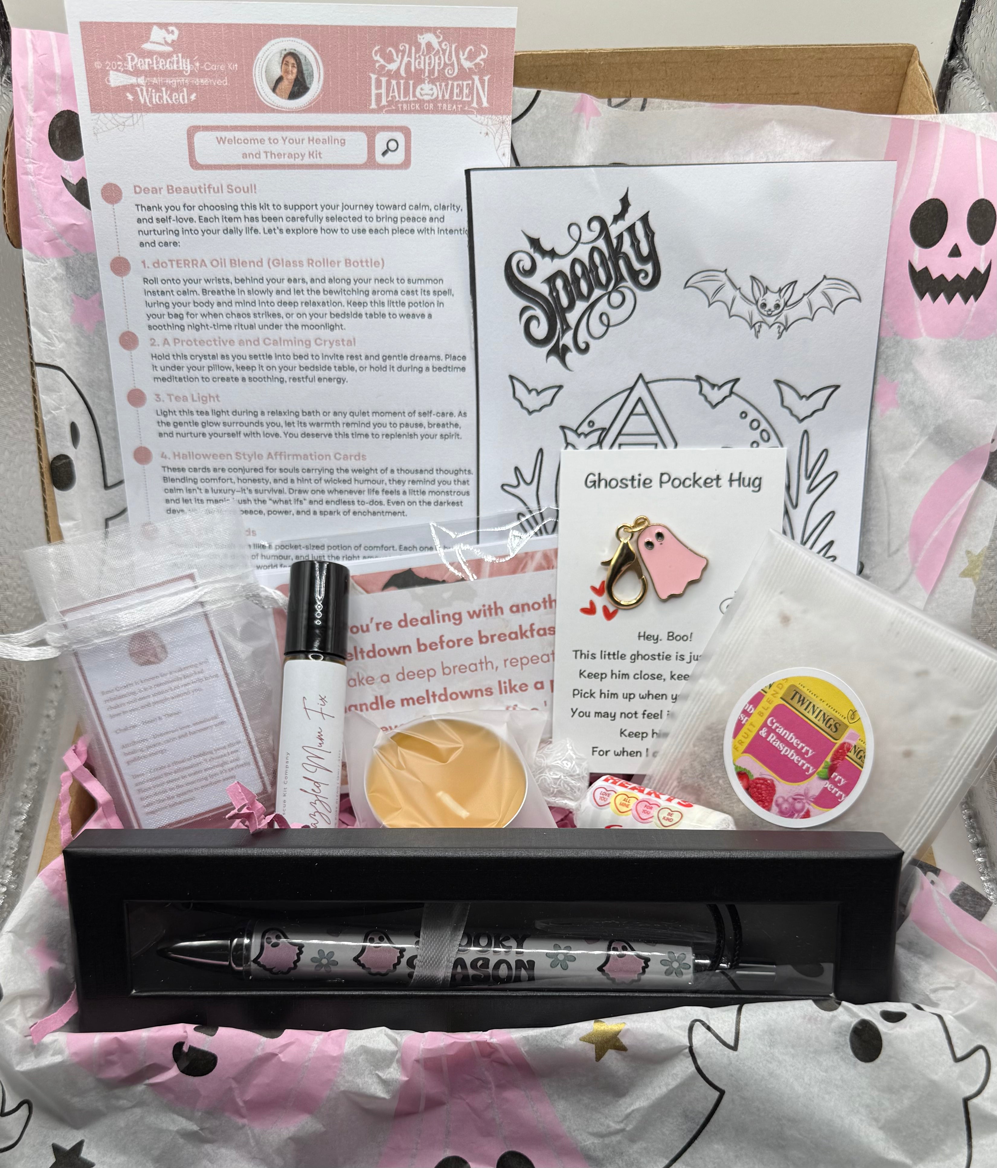 pink themed halloween kit with a pen in a black box, colouring sheet, 10ml roller blend bottle, a tea bag, tea light candle, pack of love heart sweets, a ghost pocket hug card wrapped in pink halloween paper